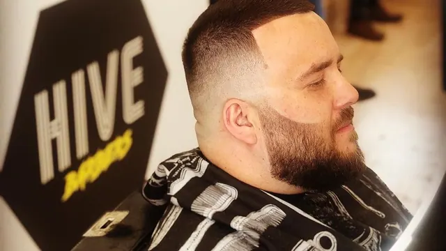 A fade and beard in front of the Hive sign
